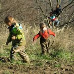 Im Vordergrund stampfen zwei Kinder durch den Matsch, währen im Hintergrund drei andere auf einen Baum klettern