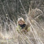 Ein blondes Mädchen trägt eine Garbe im hohen dürren Gras