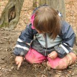 Kind malt mit Stecken im erdigen Waldboden